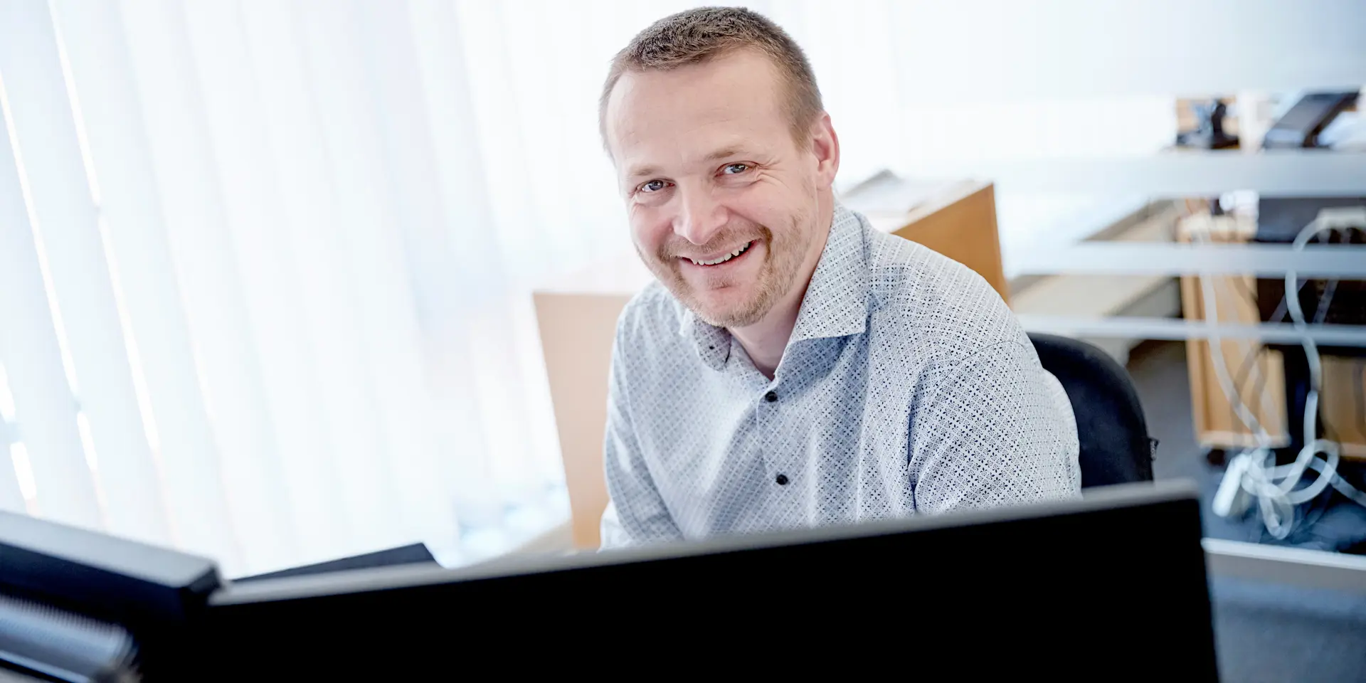 Rådgiver smiler mens han arbejder med landbrugssager i Vestjysk Bank