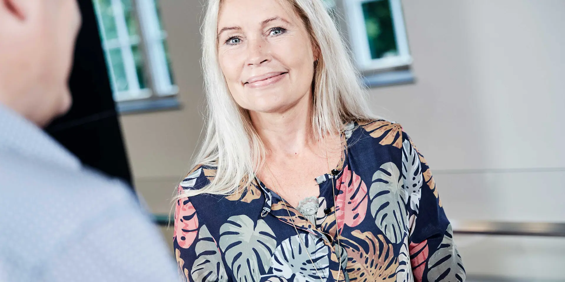 Rådgiver i blomstret skjorte og løst lyst hår smiler